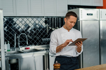 Professional chef using tablet computer for recipes while working in modern kitchen cooking concept
