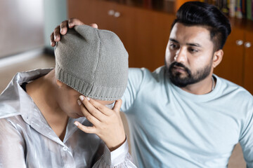 Sad and depressed south asian woman cancer patient with concealing head scarf, suffering from serious hair loss due to chemotherapy negative side effect but having family staying together for support - obrazy, fototapety, plakaty