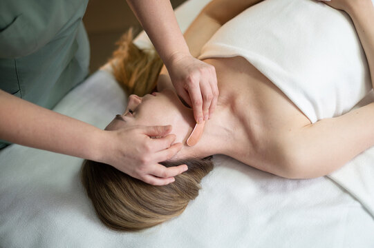 Hands of the masseur are close-up using a metal massage tool to massage the body of a woman lying on a couch. Health concept, body care, skin care, wellness