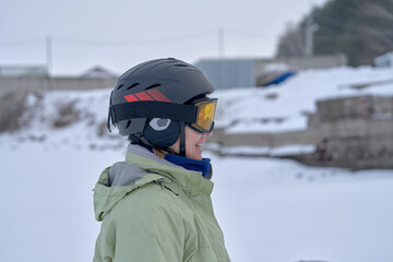 A middle-aged woman, a snowsurfer, stands and waits. Preparing to ride a sailboard in the snow on a cloudy winter day.