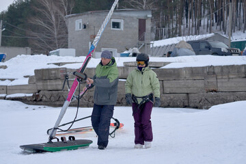 A middle-aged man and woman, snowsurfers, husband and wife, roll out a sailboard into an open area for skiing in the snow. Preparing to ride a sailboard in the snow on a cloudy winter day.
