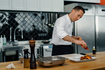 A professional chef adds spices to baked potato wedges in the process of preparing a healthy meal