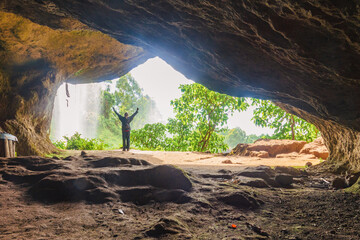 Rear view of a hiker in a cave against the background of Sipi Waterfall in Mount Elgon, Mbale,...