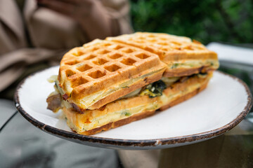 Waffle sandwich with spinach, mushrooms and cheese in a plate outdoor in sidewalk cafe. Close up. Soft focus