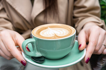 Cup of coffee cappuccino or latte in woman hands outdoors in coffee house or cafe. Classic heart shaped latte art