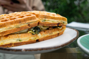 Belgian vegetarian waffle sandwich with spinach, mushrooms and cheese in a plate outdoor in sidewalk cafe