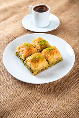 Pistachio baklava on a white plate with Turkish coffee.A plate of traditional baklava on burlap...