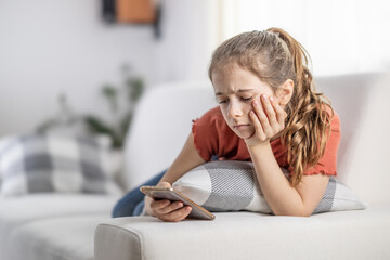 Bored young girl finds no more joy in scrolling on her phone as she sits at home on a couch