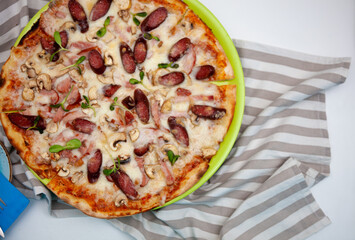 Pizza with mini sausages, bacon, meat, mushrooms and cheese. Thin homemade Italian pizza. Food background. Plate top view
