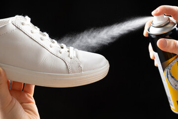 Applying a water-repellent hydrophobic spray to white women's sneakers. Protection of shoes from...
