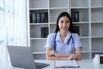 Young beautiful Asian doctor woman working happy and smile in hospital, sitting on table, Asian medical concept