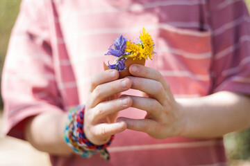 mano de niño sujetando huevo de pascua con flores amarillas y moradas. Semana santa. Horizontal. sin cara - obrazy, fototapety, plakaty