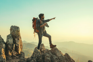 traveler with backpack and holding  binocular standing on top of mountain pointing at view