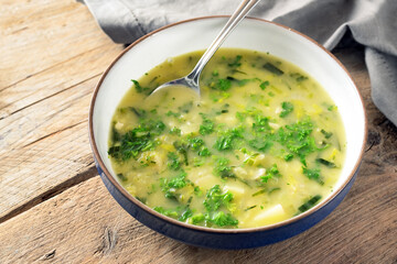 Potato parsley soup in a plate with spoon on a rustic wooden table, healthy vegetarian dish, copy...