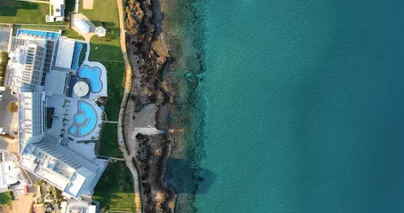 Gordijnen Drone shooting top view of the coastline with luxury hotels or villas with swimming pool, green fresh lawn, its own sandy and rocky beach and calm sea with clear blue water in Larnaca Cyprus. © Anton