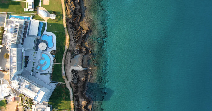 Drone shooting top view of the coastline with luxury hotels or villas with swimming pool, green fresh lawn, its own sandy and rocky beach and calm sea with clear blue water in Larnaca Cyprus.