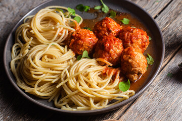 Pasta with meatballs and sauce in a plate on a wooden table