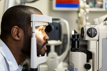 Profile view. Examination of a dark-skinned man with a slit lamp, microscope, and focused light...