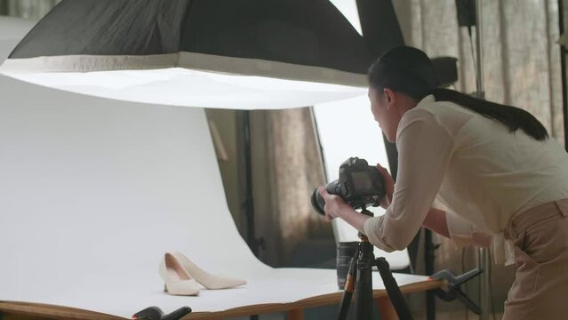 Asian Female Photographer Adjusting Position Of Women'S Shoes While Taking Photos Of Them In Home Studio 
