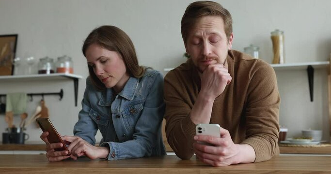 Bored ignoring silent gadget addicted couple using smartphones in kitchen, chatting, reading online content, suffering from addiction, relationship crisis, avoiding communication