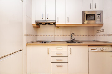 Frontal image of a kitchen with white cabinets with gray metal handles, wooden details and a matching countertop
