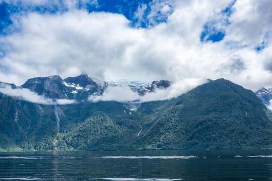 water falls and hanging glaciers seen from a boat in fjord with white clouds patagonia, aysen region, chile