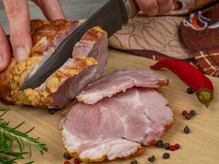 Cutting slices of juicy pork ham on a wooden cutting board with a carving knife. Close-up female hands cutting slices of juicy and tasty pork ham. The concept of cooking delicious meat products