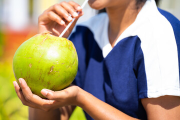Close up shot of woman drinking coconut water during summer at park after morning walk or jog -...