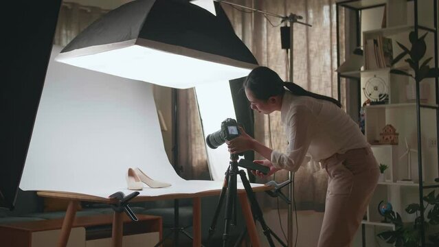Asian Female Photographer Talking On Smartphone While Taking Photos Of Women'S Shoes In Home Studio 
