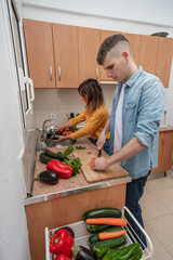 Young couple cooking together on a kitchen. Man and woman vegan cook vegetables for meal. Healthy lifestyle