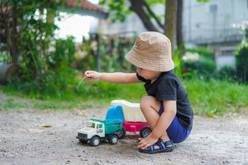little child playing with toy car on the playground. asian toddler kid boy play outside in backyard on sunny morning wearing brown hat and black shirt	