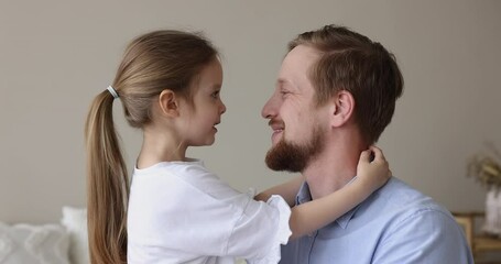 Happy handsome affectionate daddy hugging little daughter girl with nose touches, talking to kid, laughing, smiling. Father enjoying fatherhood, family leisure, cuddling cute child at home