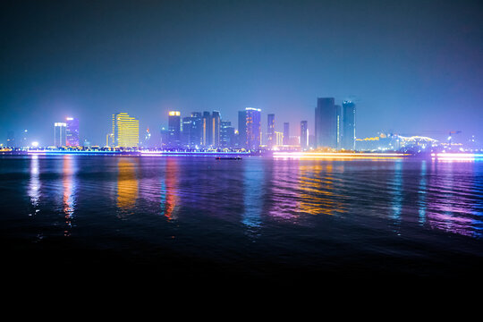 Colorful city night scene on the coast with colorful lighting water reflection in the mist. In Hangzhou, China.