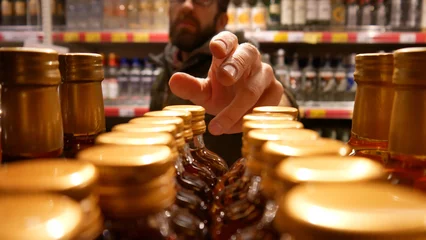 Fototapeten A man reach out to take a cognac bottle in an alcohol store © Stockah