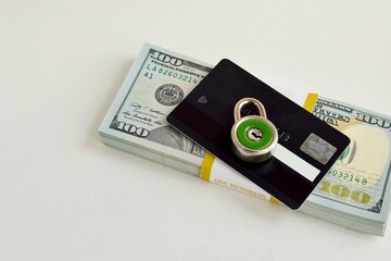 A bank card under lock on a stack of US hundred dollar bills. The concept of security and protection of bank cards.