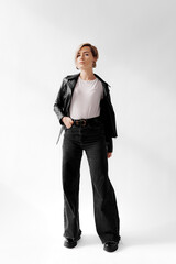 Full body of self assured young female with blond hair model standing with hand in pant pocket and looking at camera against white background