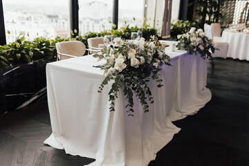 Head table at wedding. Table for groom and bride decorated with white roses and greenery. 