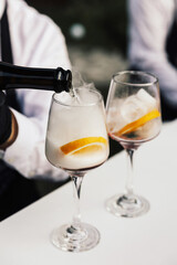 Bartender pours a sparkling wine in glass. Two glasses of cocktails on the table in the bar. 
