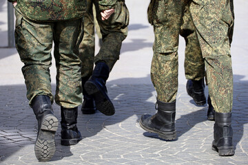 Legs of soldiers of military forces in camouflage, men in boots walking down the city street