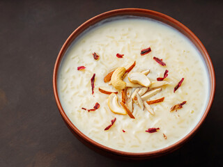 Creamy rice Kheer garnished with nuts and hibiscus. Bowl with rice pudding on dark background. Top view