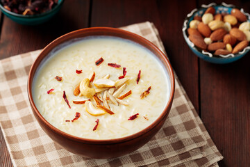 Rice pudding served in clay bowl. Indian rice kheer with nuts on a wooden background. Popular Ramadan dish. Top view