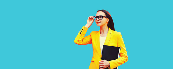 Portrait of young woman with folder wearing eyeglasses, yellow business suit on blue background