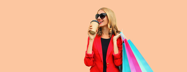 Portrait of beautiful happy smiling young woman with colorful shopping bags and cup of coffee wearing business blazer on pink background