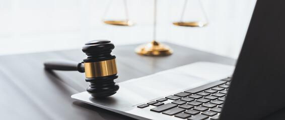 Symbolizing justice and legal authority, golden balanced scale and gavel on desk with laptop in law...