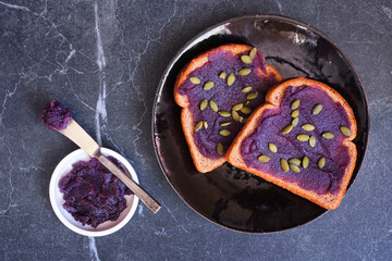 Toast with ube halaya jam and pumpkin seeds. Sweet, trendy, purple yam spread. Above view table scene on a dark slate background.