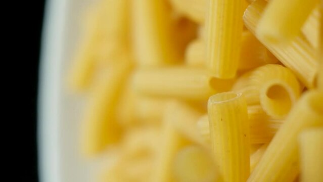 Flying wheat pasta Rigatoni in the form of tubes fall from top to bottom, close-up, slow motion shooting.