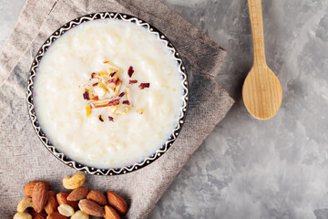 Indian rice kheer with nuts on a gray background. Bowl with rice pudding and a linen napkin on...