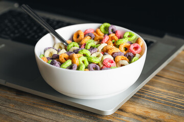 Colored breakfast cereals in a bowl and laptop, workplace breakfast, quick healthy breakfast in the office in the morning.