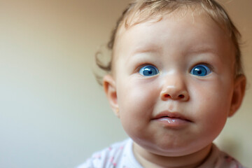 Blond baby girl face indicating surprise, wide open blue eyes with plump cheeks