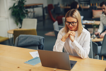 Smiling businesswoman working on laptop in coworking on colleagues background
